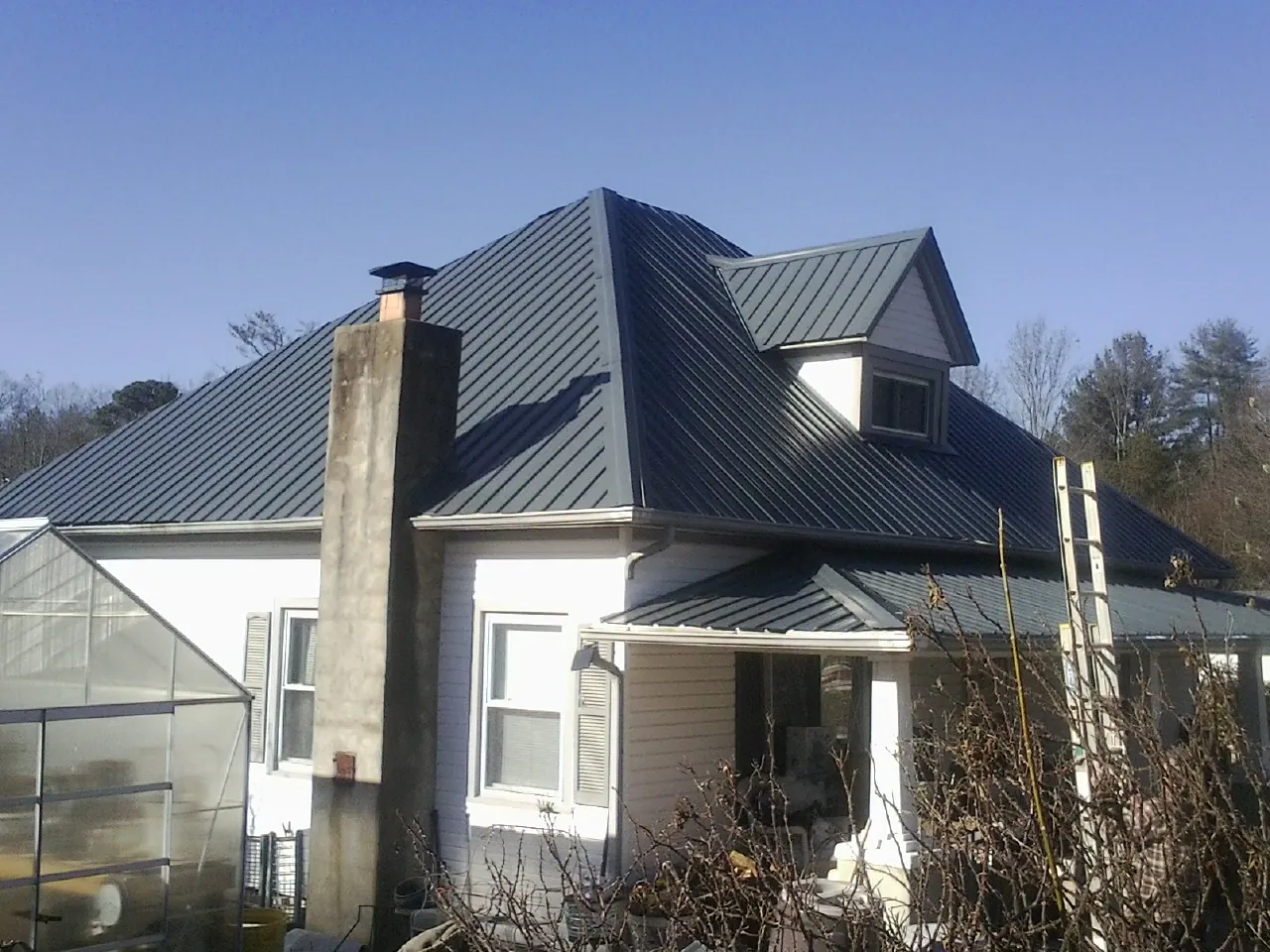 Dark blue standing seam metal roof on a white farmhouse with dormer — Slate & Tile Roof Repair by Roofing Brothers in Kanawha