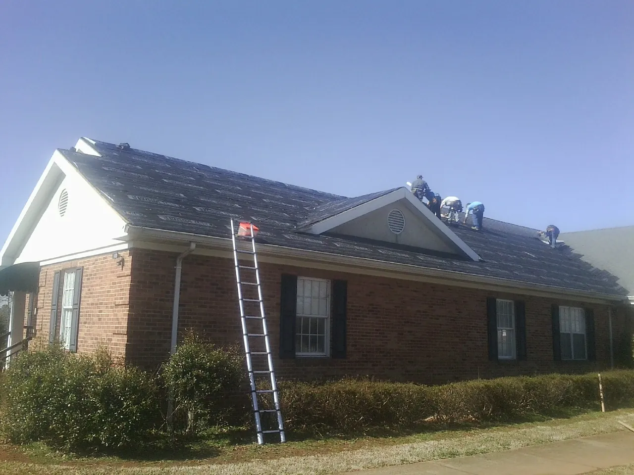 Crew tearing shingles off a brick ranch roof with a ladder set — Emergency Roof Repair work by our crew in Kanawha