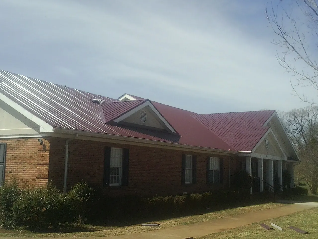Red metal roof with gabled entries on a long brick building, from a Hail Damage Roof Repair job in Kanawha