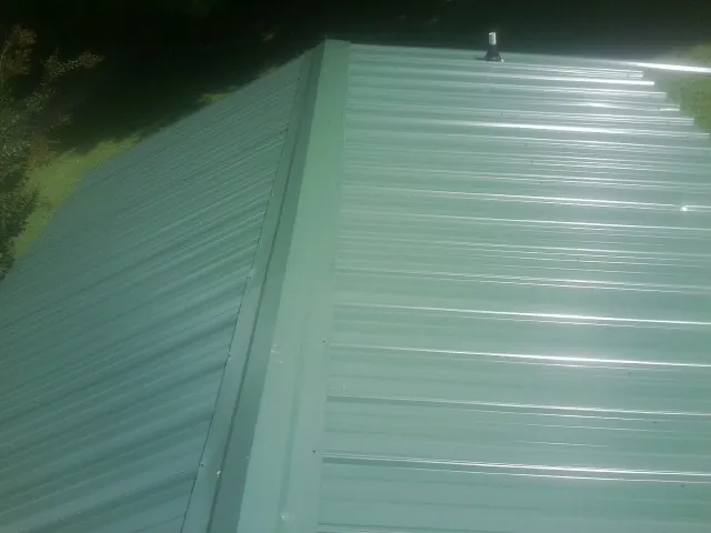 New green metal panels meeting at the ridge of a roof — Flat Roof Repair work by our crew in Kanawha