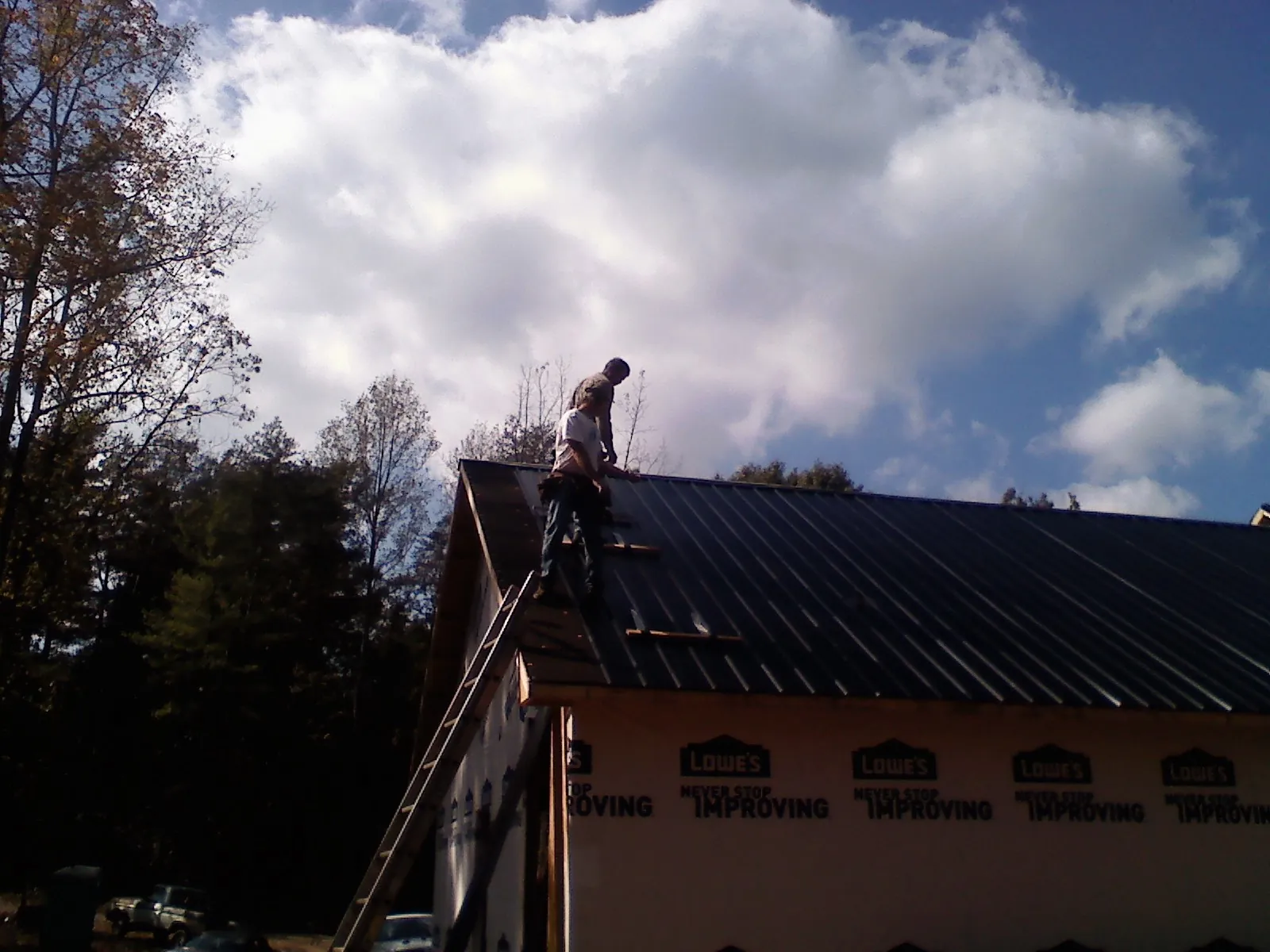Roofer fastening dark metal panels high against a cloudy sky, from a Roof Inspection job in Kanawha