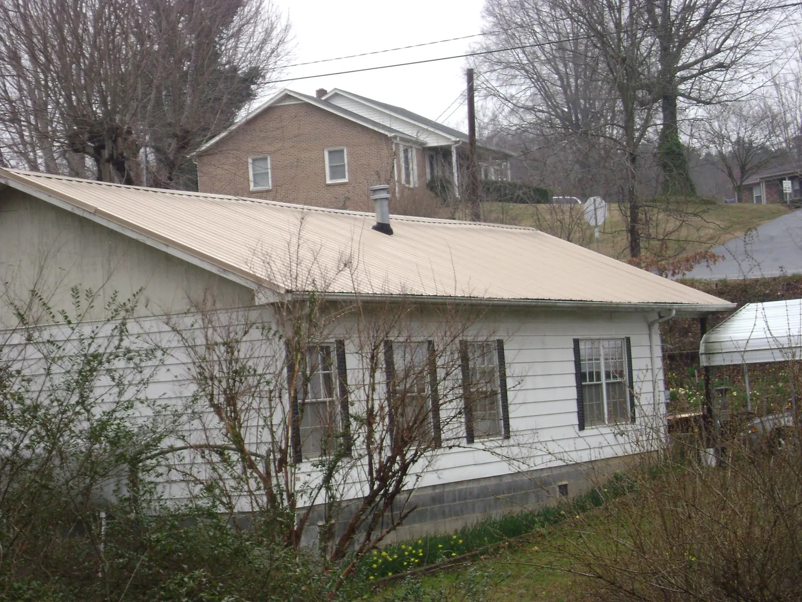 Tan metal roof on a white sided house set into a hillside — Commercial Roofing by Roofing Brothers in Kanawha